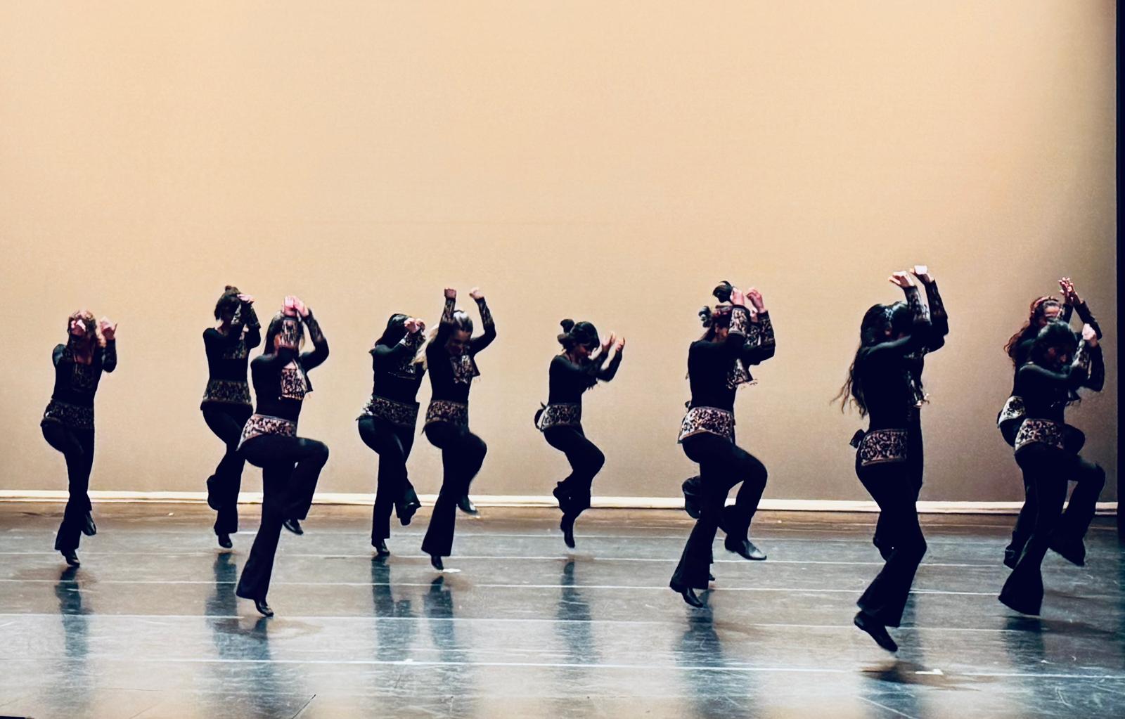Dancers mid-leap in black and gold costumes