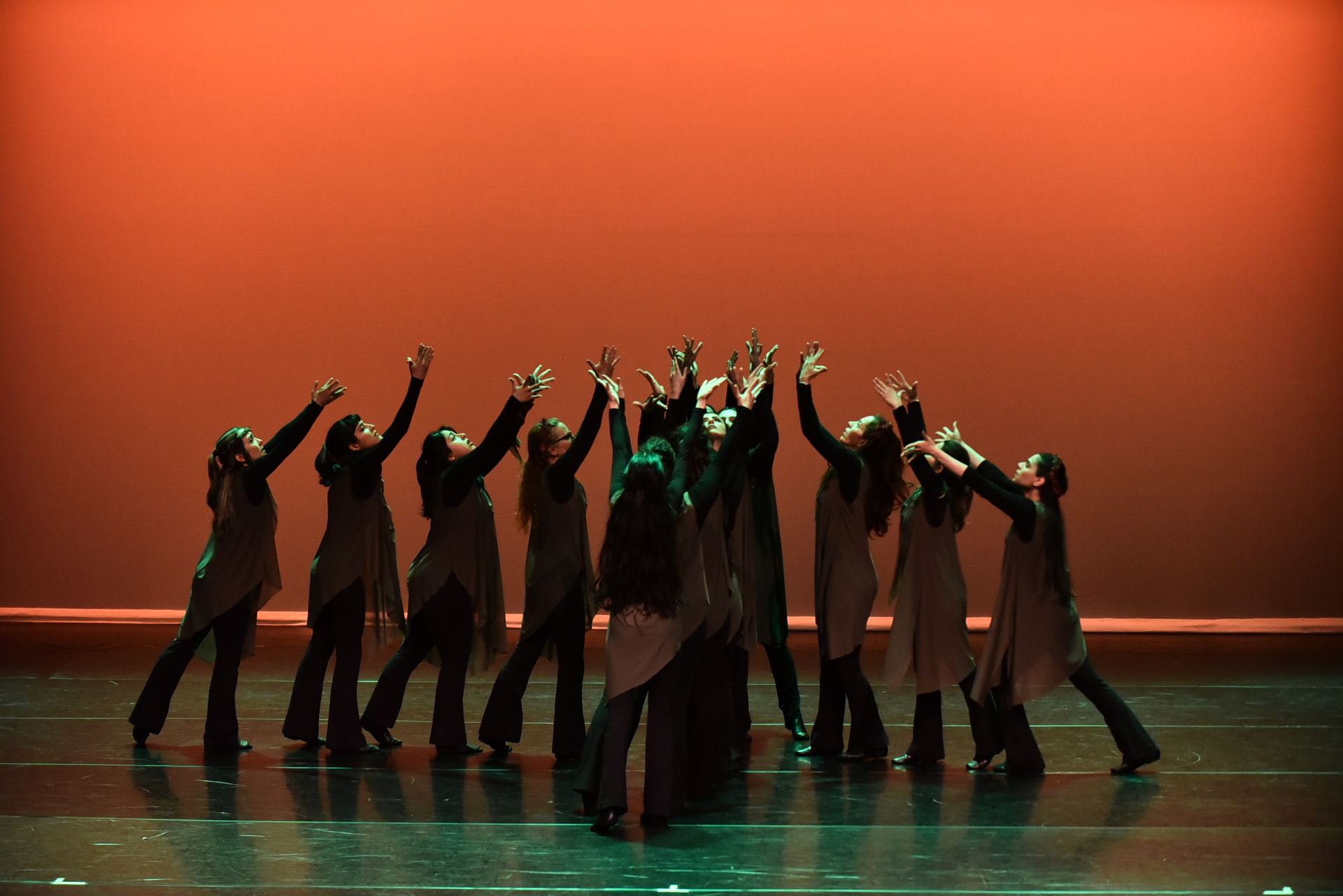 The ensemble reaching upward against a warm orange backdrop